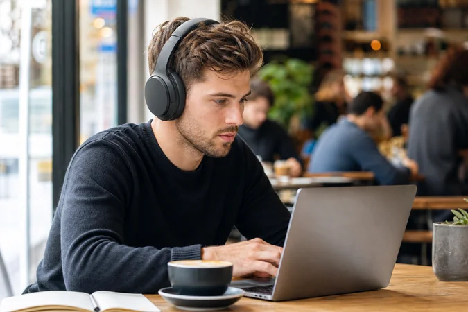 Persona con auriculares circumaurales en cafe enfocado en portátil central