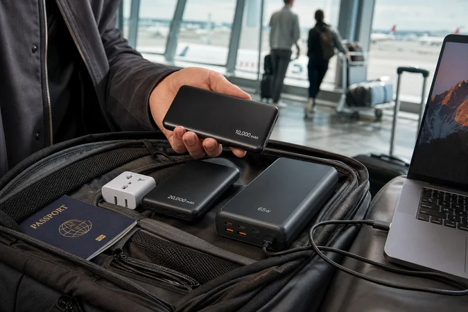 Viajero compara tres power banks en aeropuerto junto a portátil pasaporte y adaptador de viaje