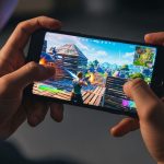 Joven jugando Fortnite en smartphone iluminado en habitación oscura