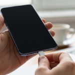 Manos sosteniendo smartphone Xiaomi con pantalla negra conectando cable USB-C